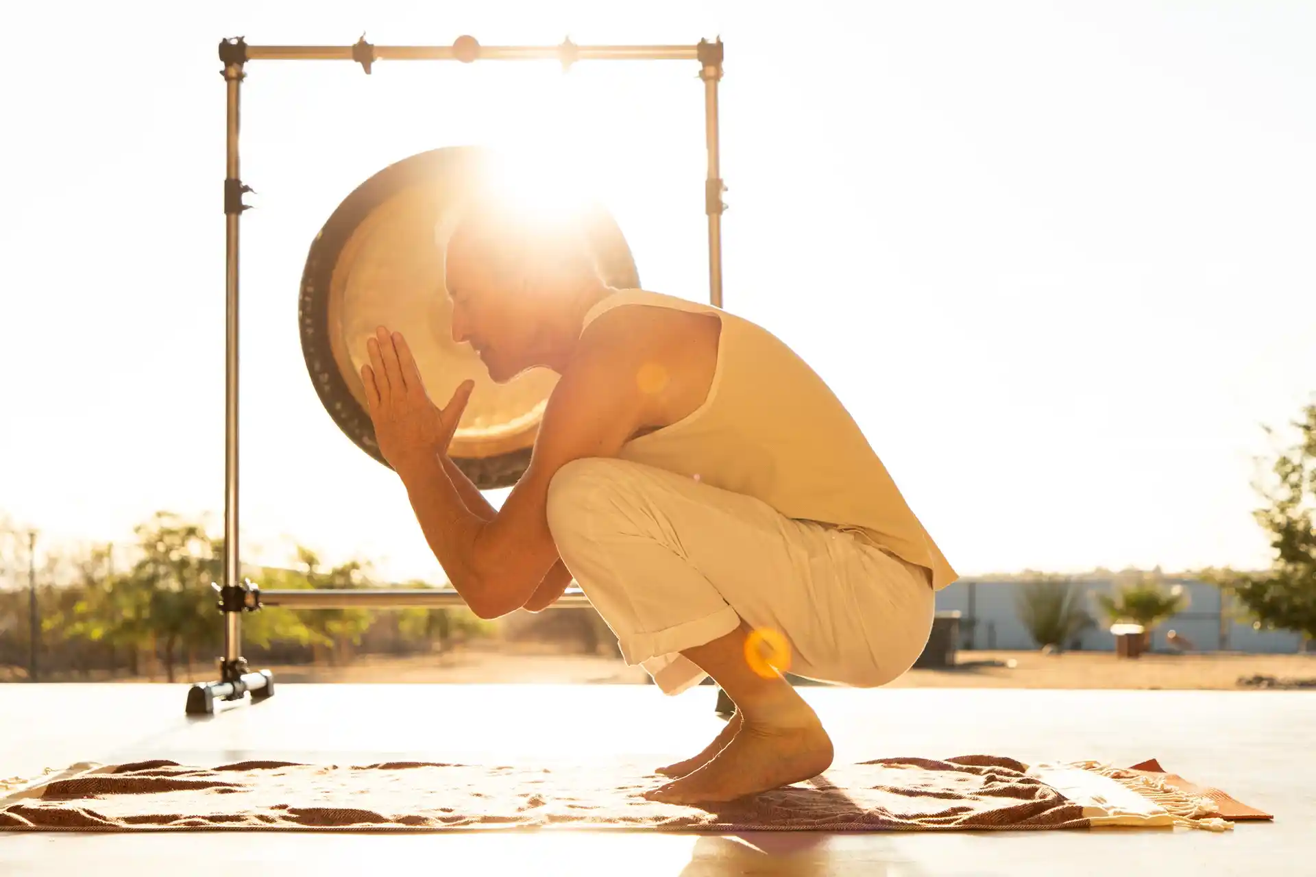 Man practicing mindful movement beside a large gong during an outdoor sound healing session in Joshua Tree.