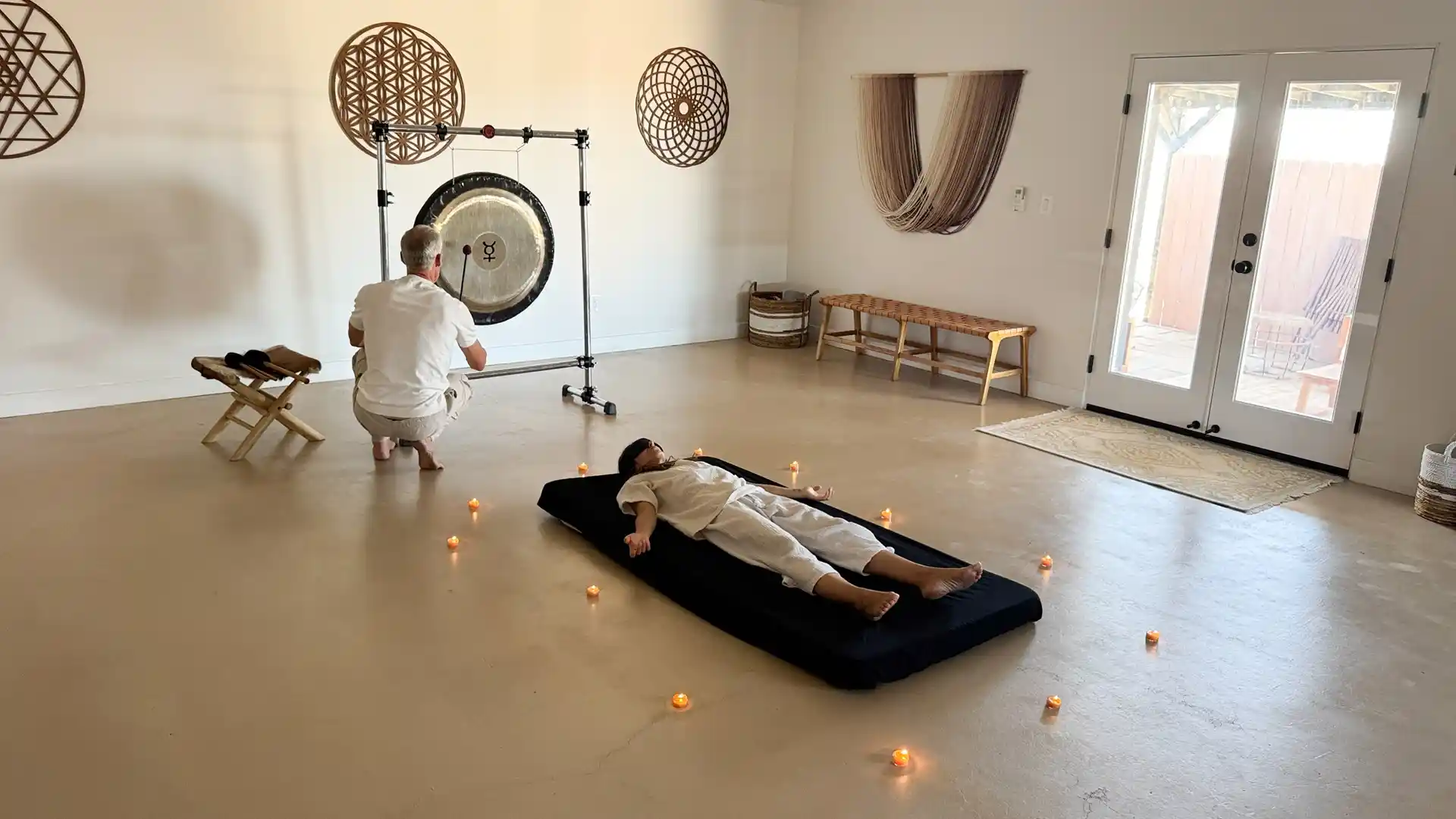Sound healing session with a gong and a participant lying on a mat surrounded by candles at Camp Vortex Retreats.
